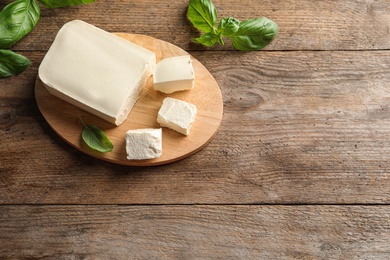 Board with feta cheese and basil on wooden background, top view. Space for text