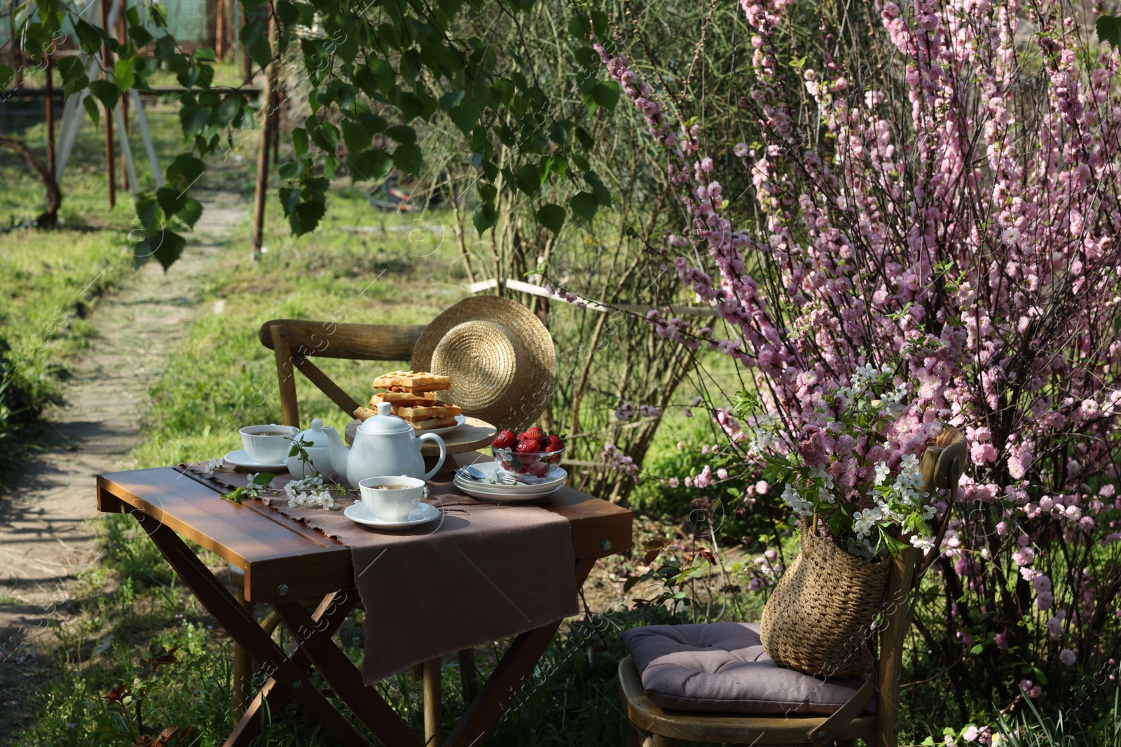 Photo of Beautiful spring flowers, freshly baked waffles and ripe strawberries on table served for tea drinking in garden