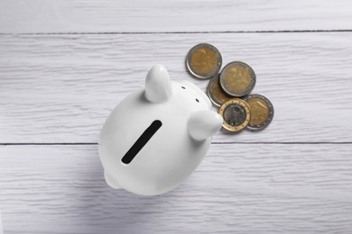 Ceramic piggy bank and coins on white wooden table, flat lay. Financial savings