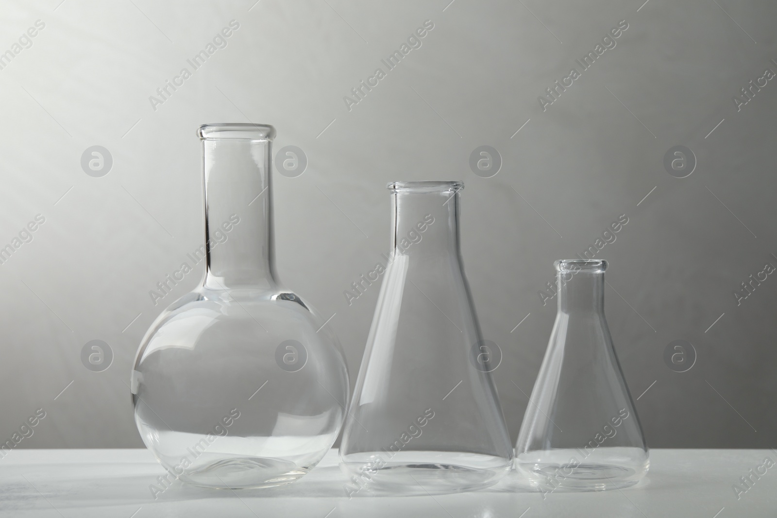 Photo of Set of laboratory glassware on white table against grey background