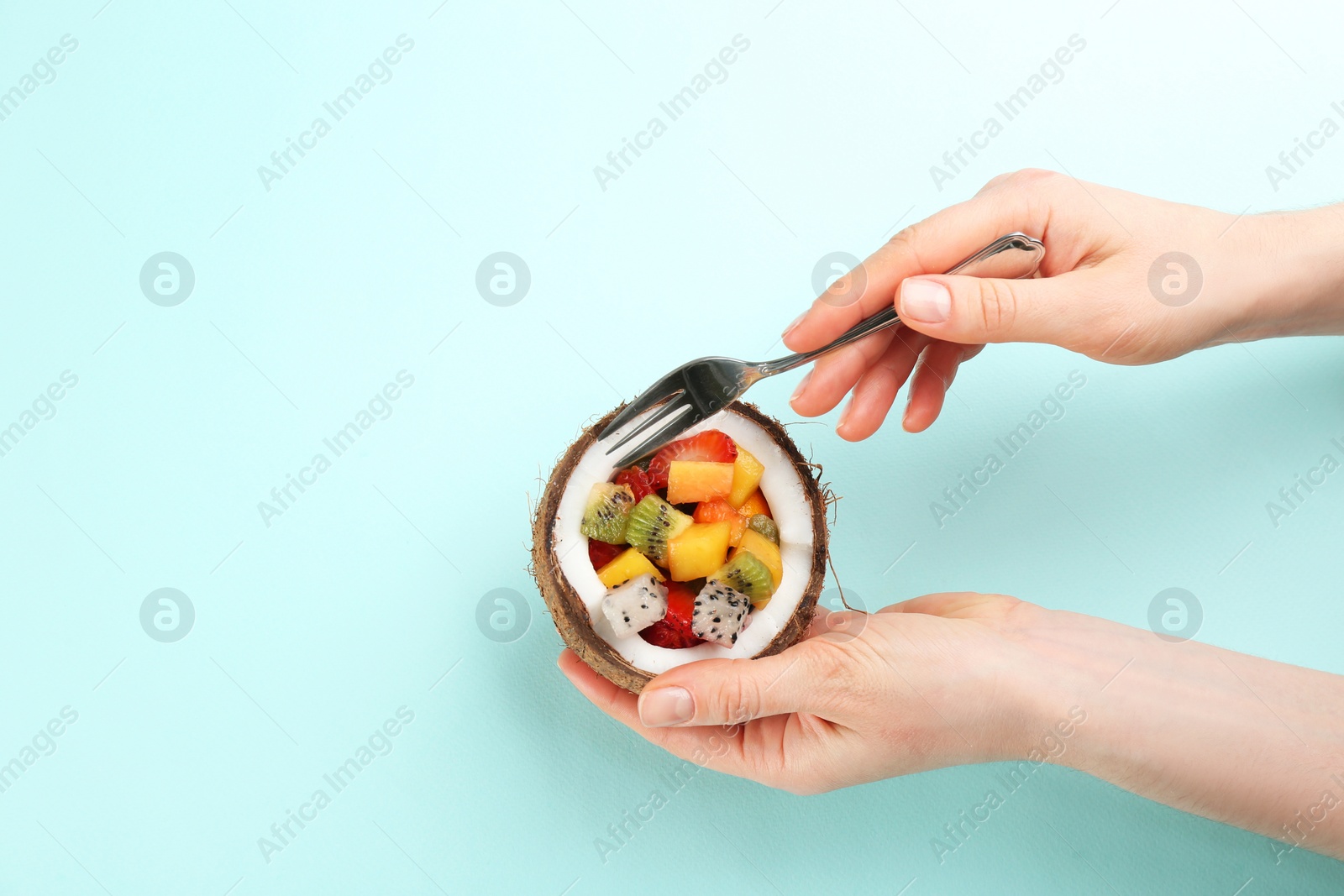 Photo of Woman with delicious exotic fruit salad on turquoise background, top view