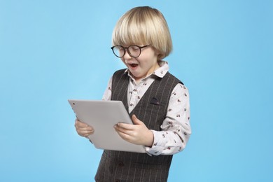 Photo of Cute little boy in glasses using tablet on light blue background