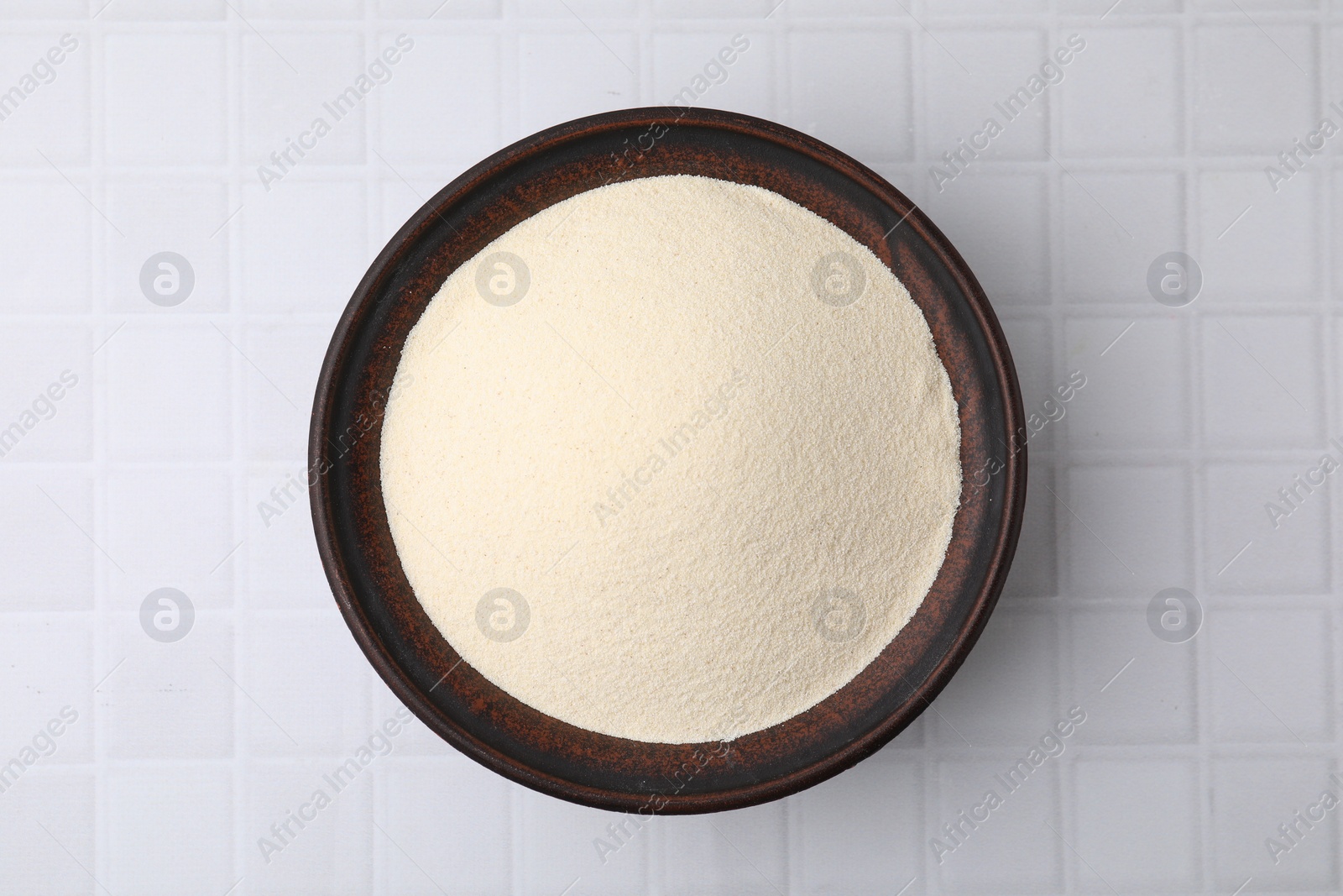 Photo of Uncooked organic semolina in bowl on white tiled table, top view