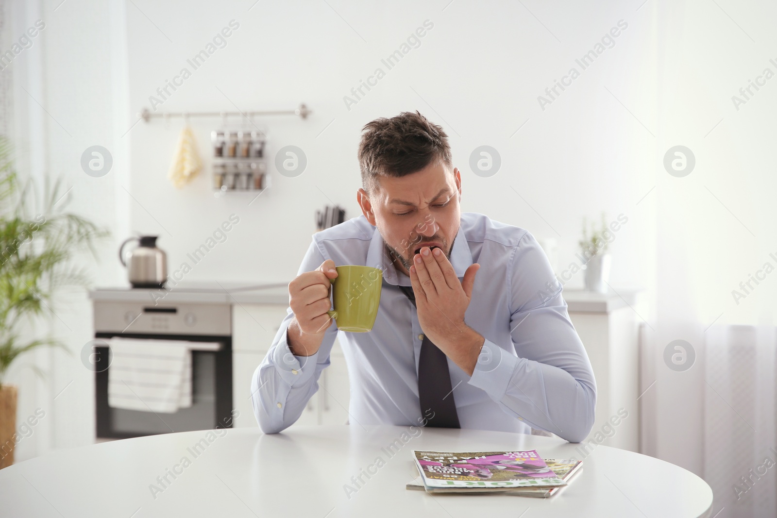 Photo of Sleepy man with cup of drink at home in morning