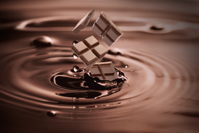 Yummy melted chocolate splashing with falling pieces as background