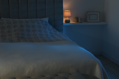 Photo of Large bed and shelf with accessories in stylish bedroom at night