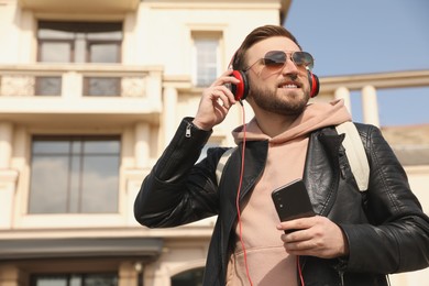 Photo of Happy young man with headphones and mobile phone listening to music on city street