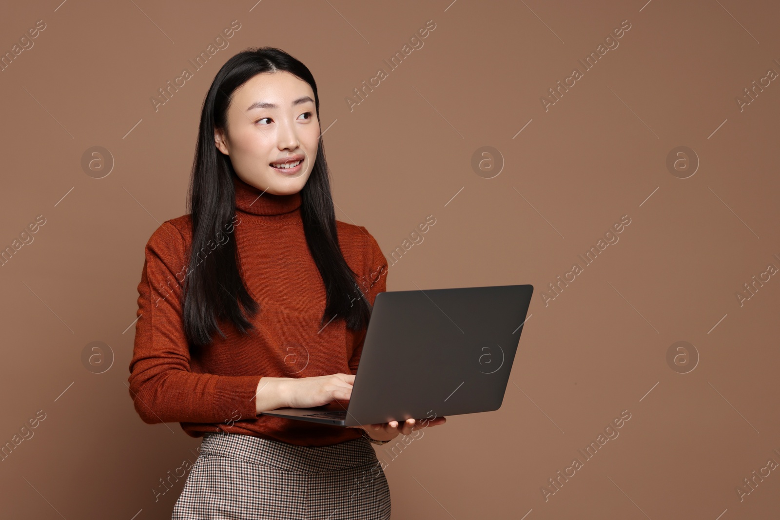 Photo of Portrait of smiling woman with laptop on brown background. Space for text