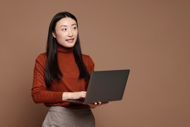 Portrait of smiling woman with laptop on brown background. Space for text