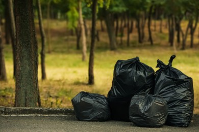 Trash bags full of garbage on pavement in park. Space for text