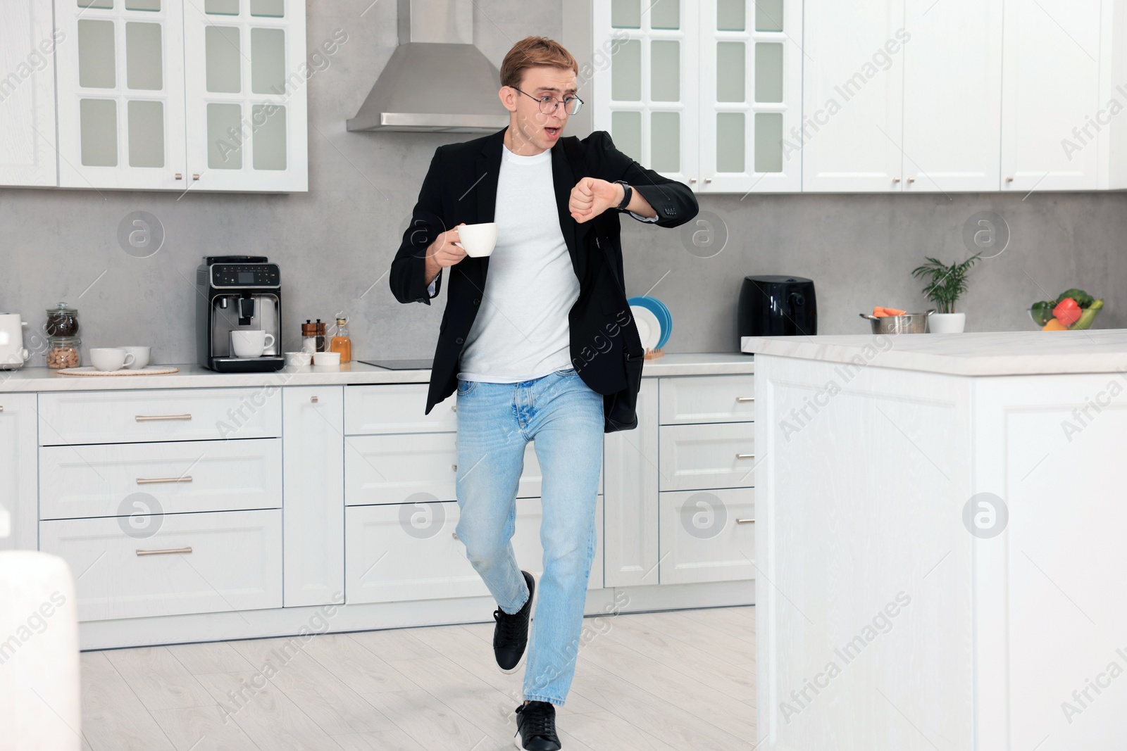 Photo of Emotional young man checking time while drinking coffee in kitchen. Being late