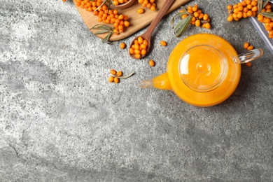 Photo of Delicious sea buckthorn tea and fresh berries on grey table, flat lay. Space for text