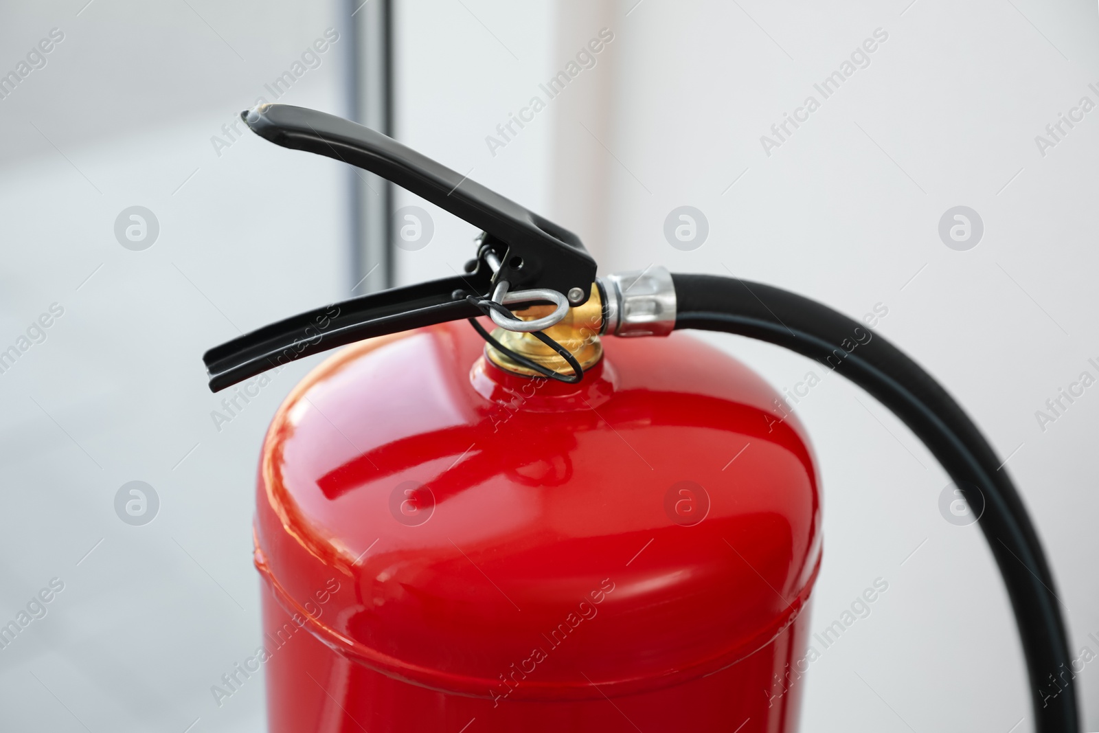 Photo of Modern fire extinguisher near window indoors, closeup