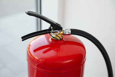 Photo of Modern fire extinguisher near window indoors, closeup