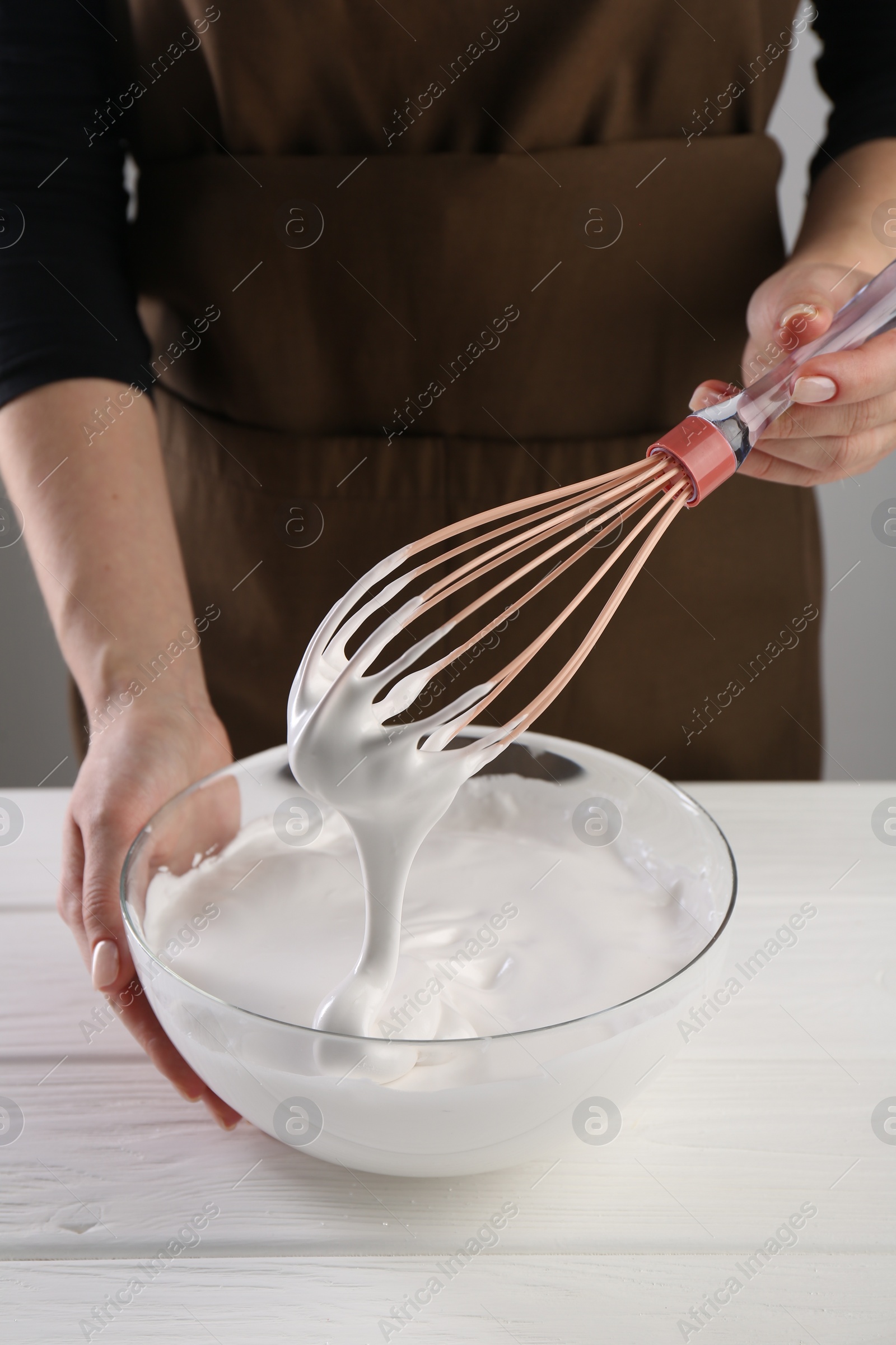 Photo of Woman making whipped cream with whisk at white wooden table, closeup