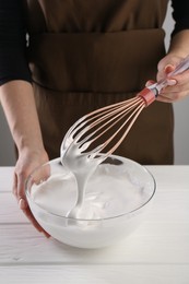 Woman making whipped cream with whisk at white wooden table, closeup