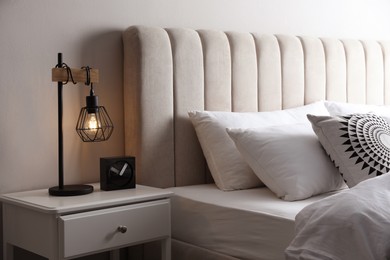 Photo of Stylish lamp and alarm clock on bedside table indoors. Bedroom interior elements