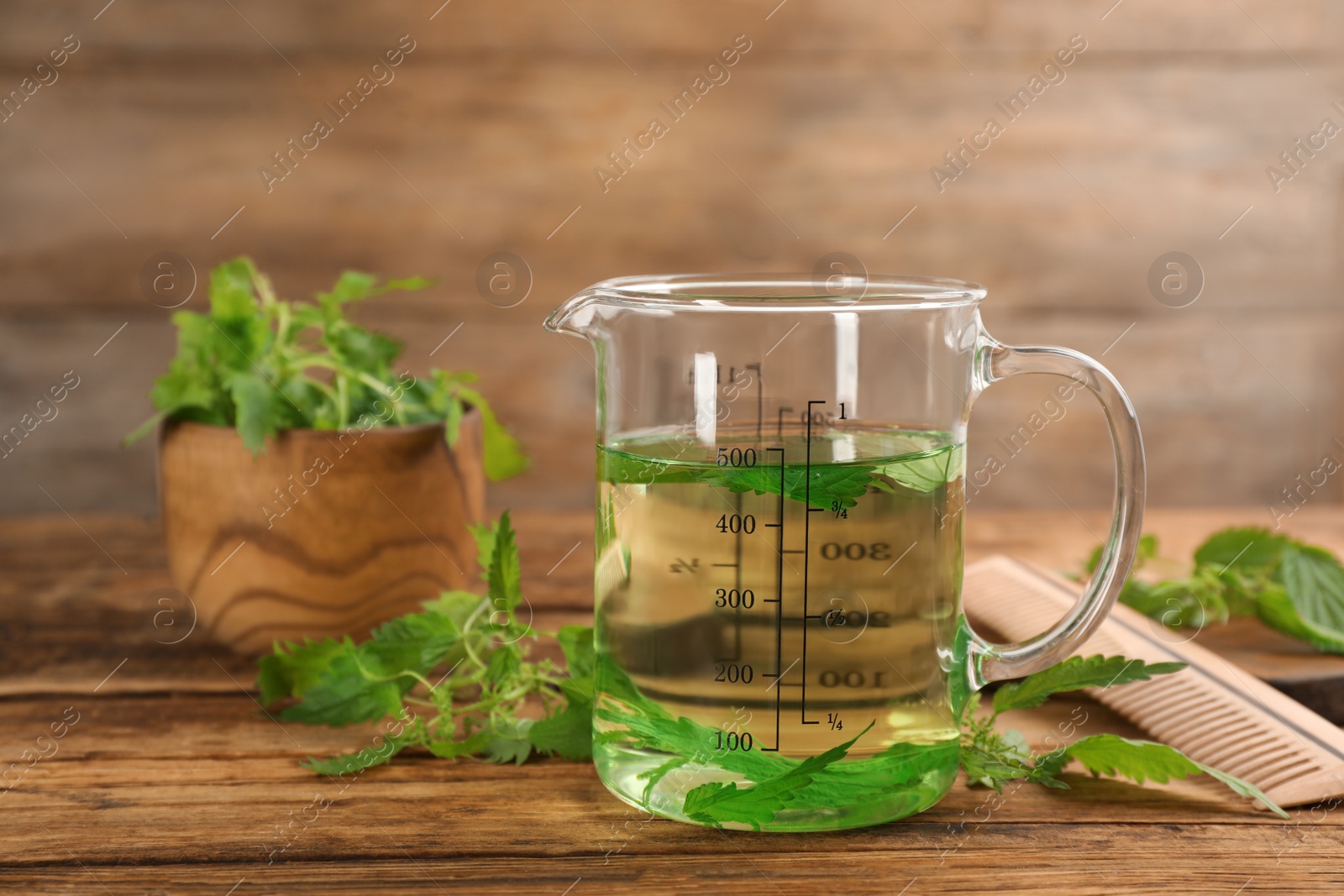 Photo of Stinging nettle extract and leaves on wooden background. Natural hair care