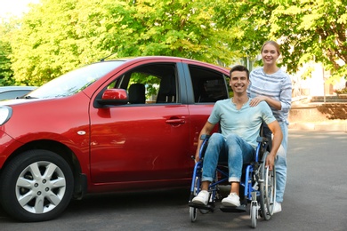 Photo of Young woman with disabled man in wheelchair near car outdoors