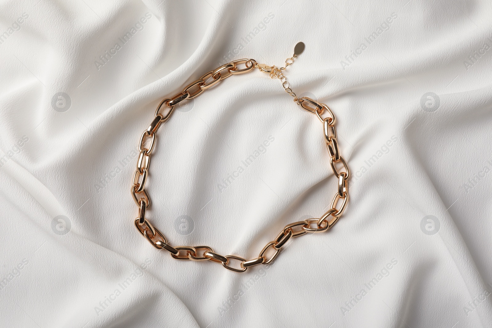 Photo of Elegant golden necklace on white fabric, top view. Stylish bijouterie