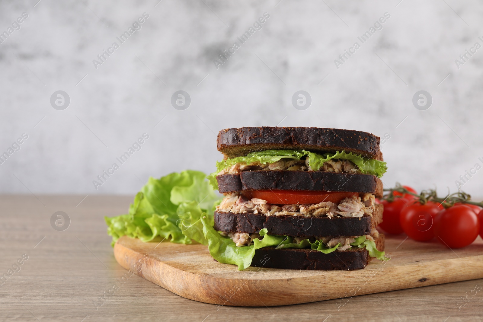 Photo of Delicious sandwich with tuna, tomatoes and lettuce on wooden table, space for text