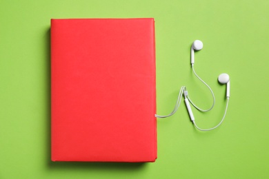Paper book and headphones on green background, flat lay