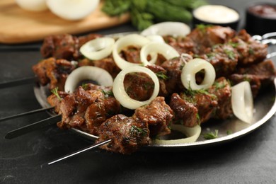Metal skewers with delicious meat and onion served on black table, closeup