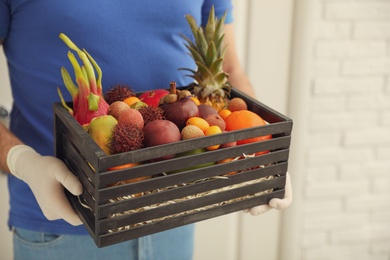 Photo of Courier holding crate with assortment of exotic fruits indoors, closeup