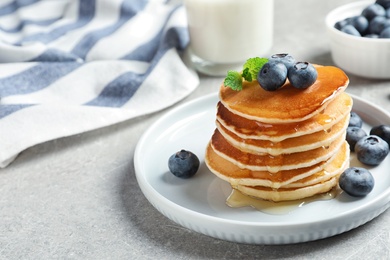 Photo of Plate of tasty pancakes with blueberries and honey on light grey table