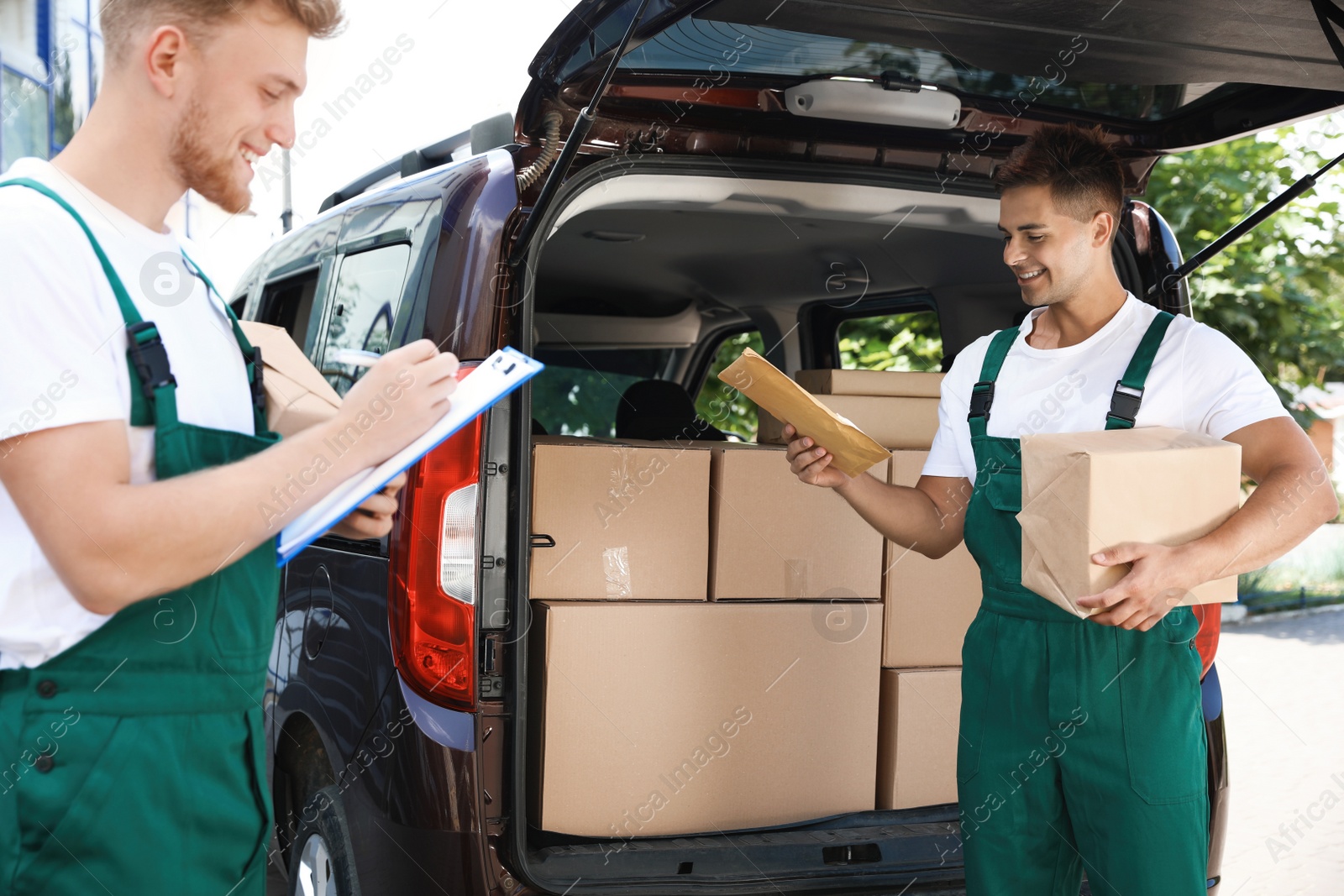 Photo of Young couriers with parcels near delivery car outdoors