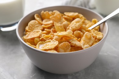 Photo of Spoon in bowl with tasty cornflakes and milk on light grey table, closeup