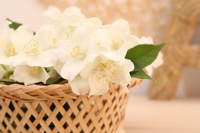 Beautiful jasmine flowers in wicker basket on table, closeup