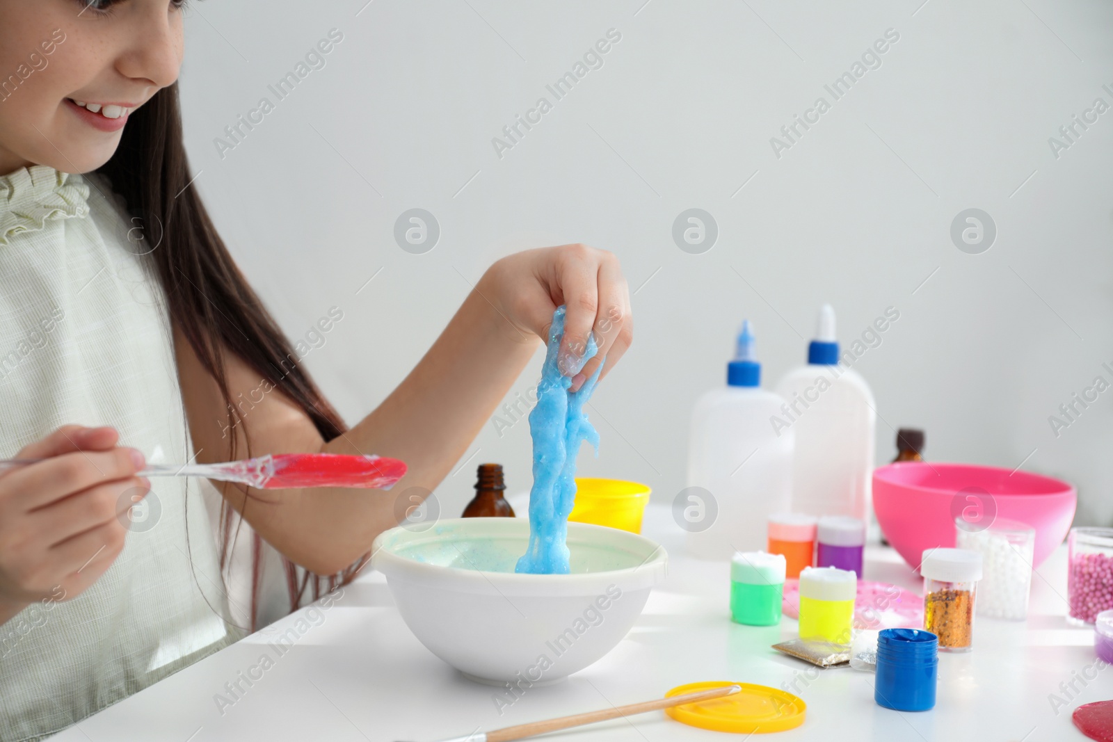 Photo of Little girl making DIY slime toy at table in room, closeup