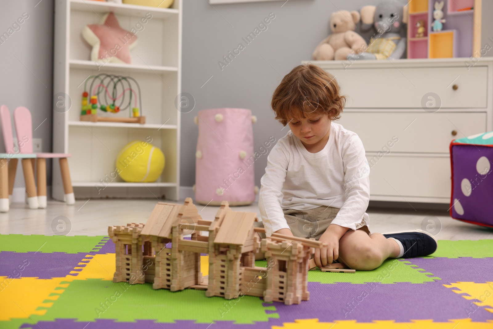 Photo of Little boy playing with wooden entry gate on puzzle mat in room. Child's toy