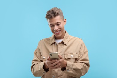 Photo of Happy young man sending message via smartphone on light blue background