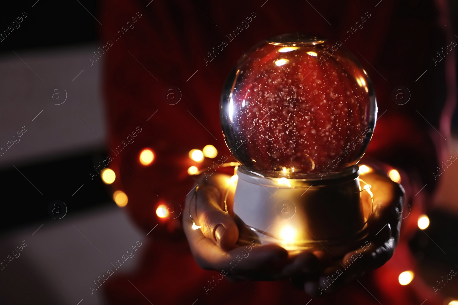 Photo of Woman holding snow globe and Christmas lights, closeup. Space for text