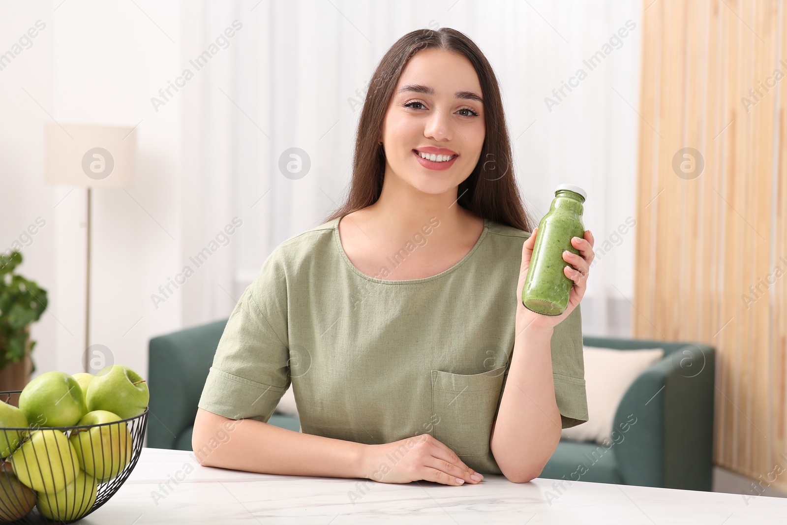 Photo of Beautiful woman with bottle of delicious smoothie at table indoors