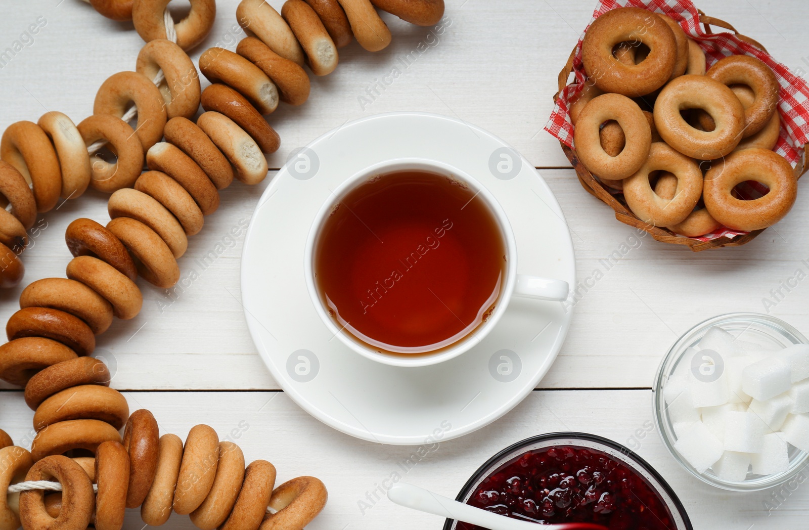 Photo of Flat lay composition with delicious ring shaped Sushki (dry bagels) and cup of tea on white wooden table