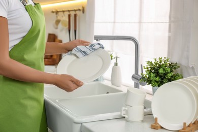 Photo of Woman wiping plate with towel in kitchen, closeup