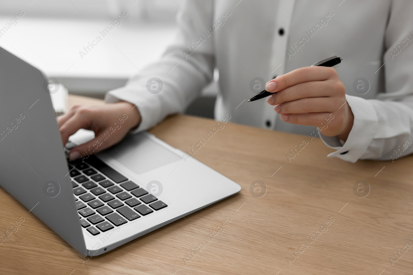 Photo of Woman with pen working on laptop at wooden table, closeup. Electronic document management