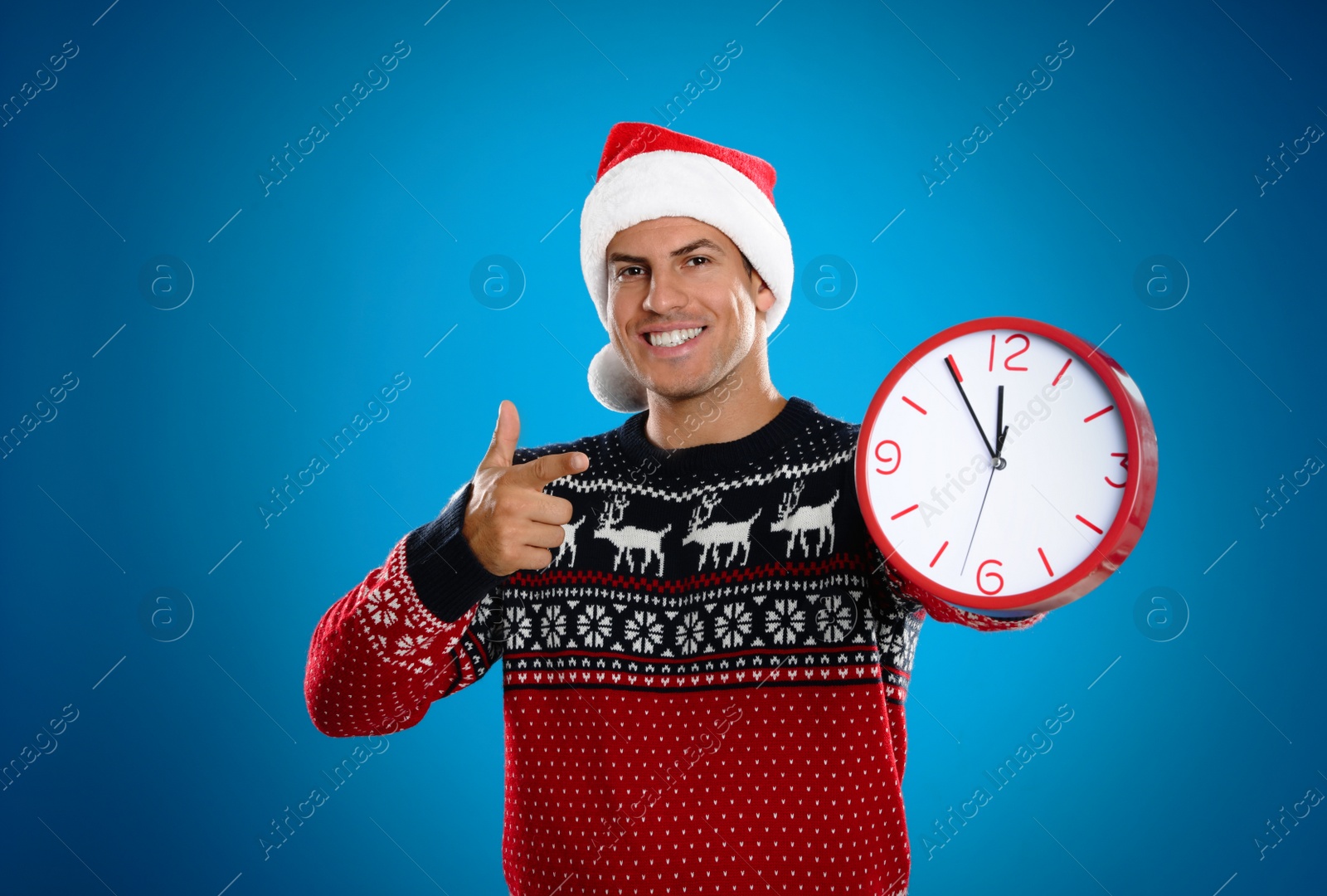 Photo of Man in Santa hat with clock on blue background. New Year countdown