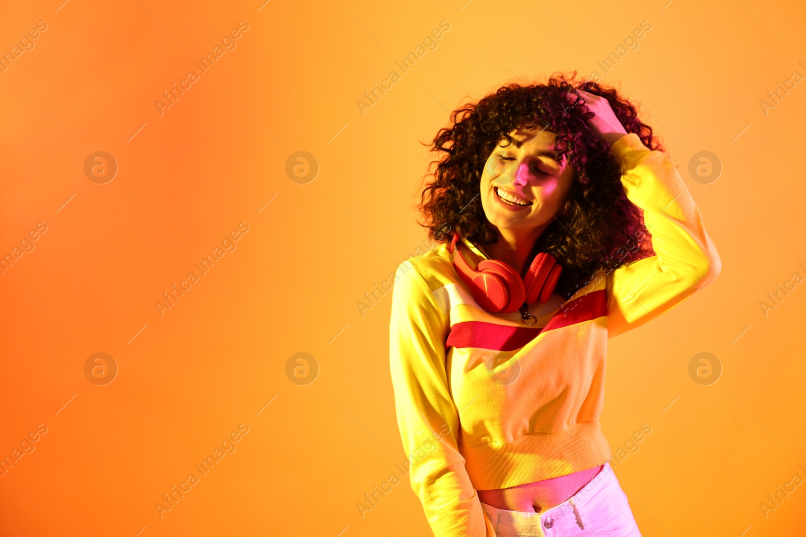 Photo of Beautiful young woman with headphones on color background in neon lights. Space for text