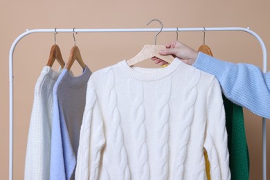 Photo of Woman holding hanger with knitted sweater against beige background, closeup