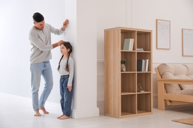 Photo of Father measuring height of his daughter near wall at home