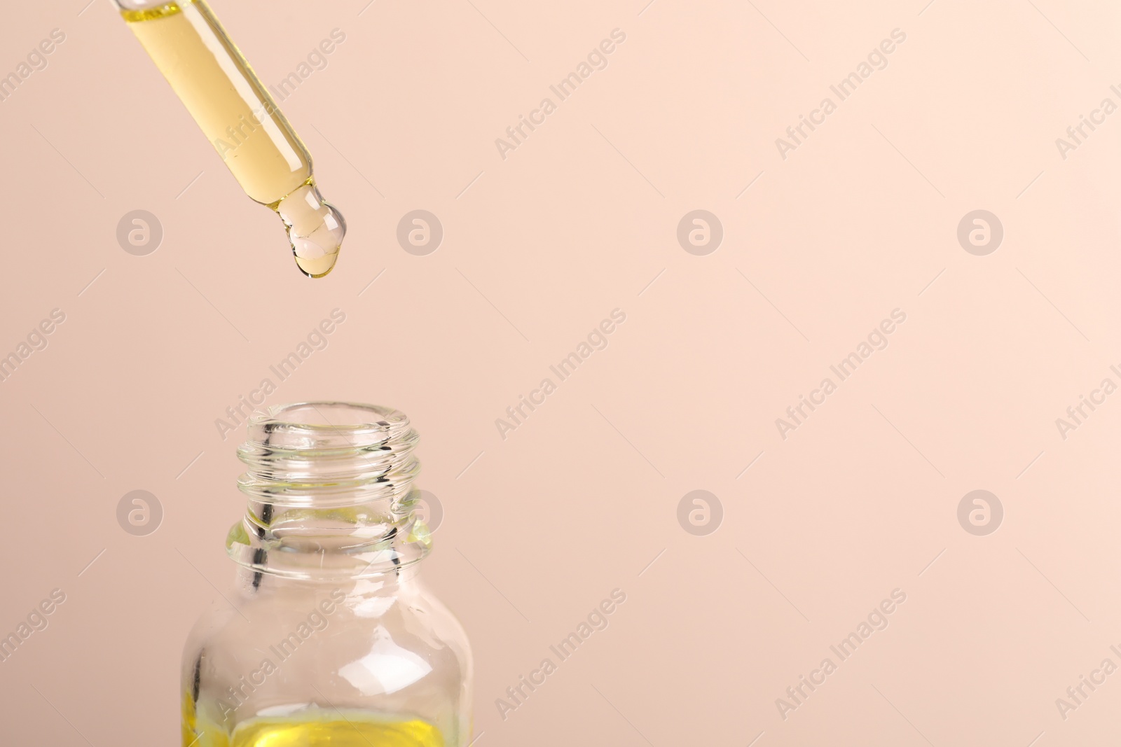Photo of Dripping cosmetic serum from pipette into bottle on beige background, space for text