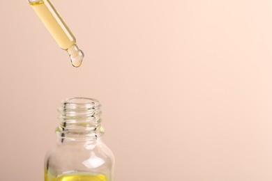 Photo of Dripping cosmetic serum from pipette into bottle on beige background, space for text