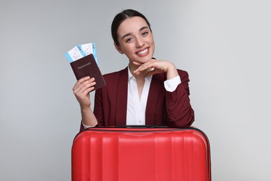 Happy businesswoman with passport, tickets and suitcase on grey background