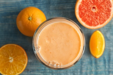 Photo of Glass with healthy detox smoothie and citrus fruits on wooden background, top view