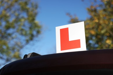 Photo of L-plate on car outdoors, low angle view with space for text. Driving school