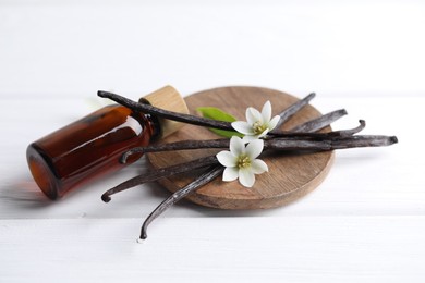 Photo of Vanilla pods, flowers and bottle with essential oil on white wooden table, closeup